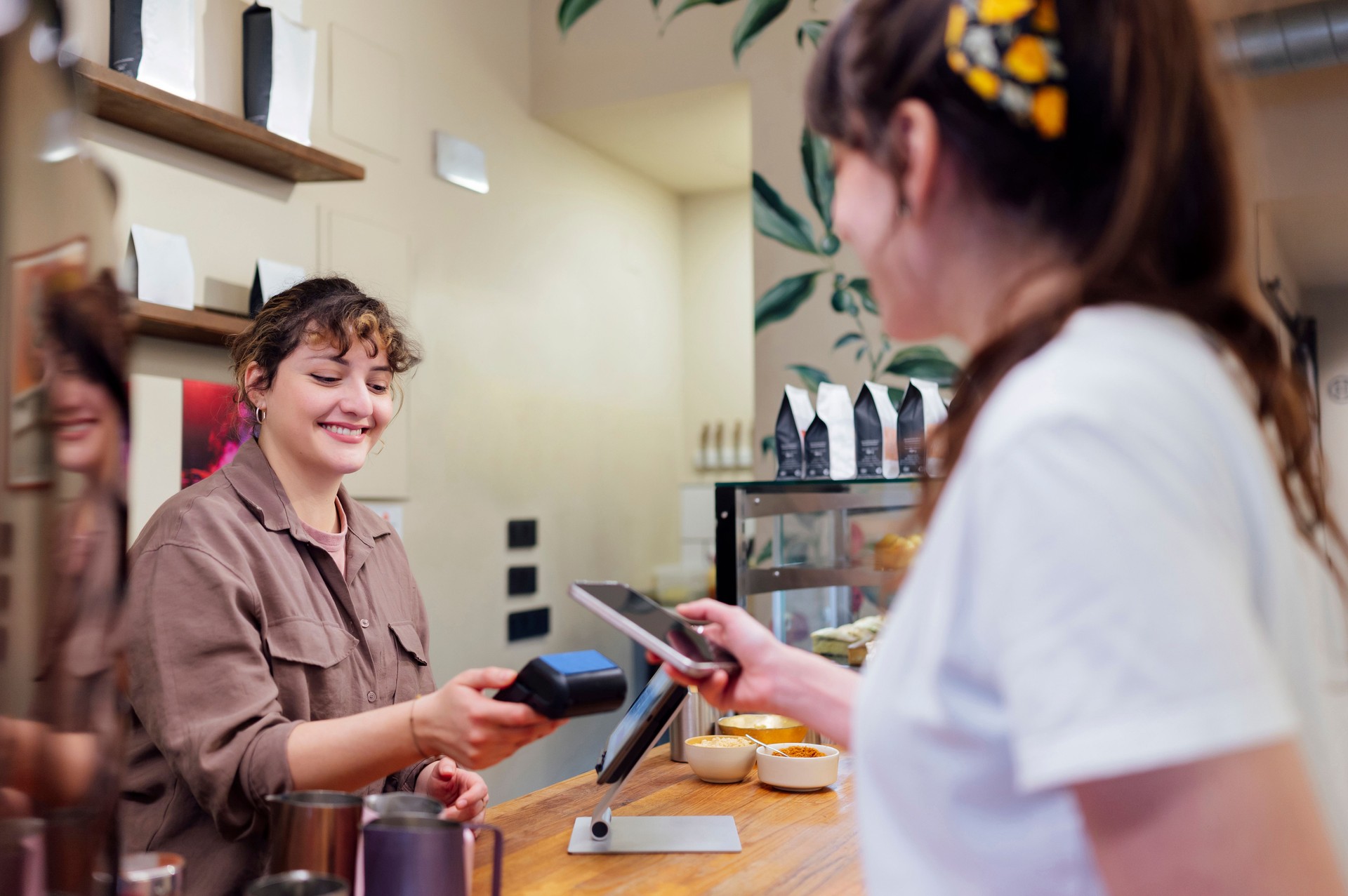 Smiling barista holding POS terminal while customer paying with smartphone using NFC technology